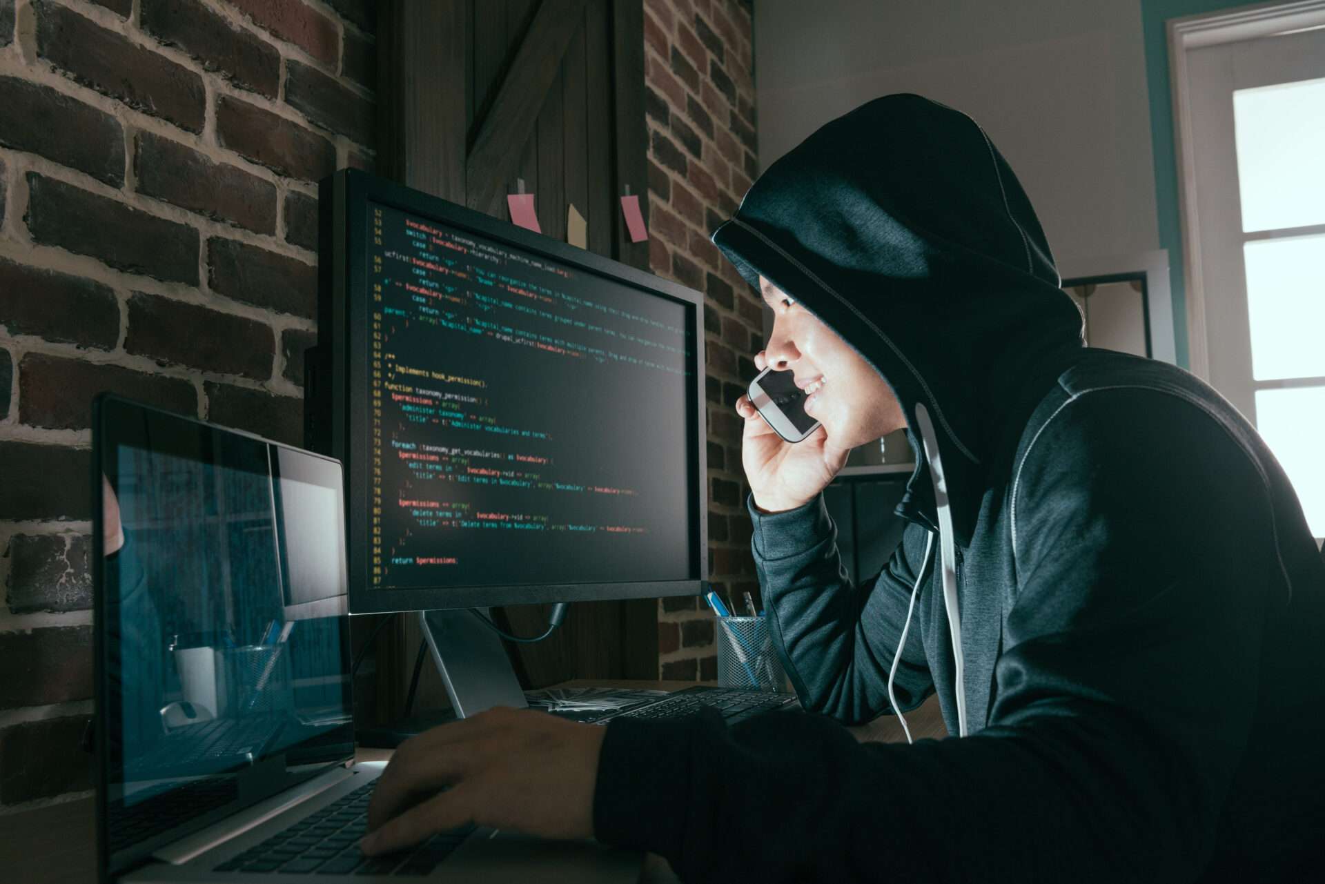 パーカーを着た男性が、コンピューターを使いながら日本語で電話でマルチタスクをこなしています。
