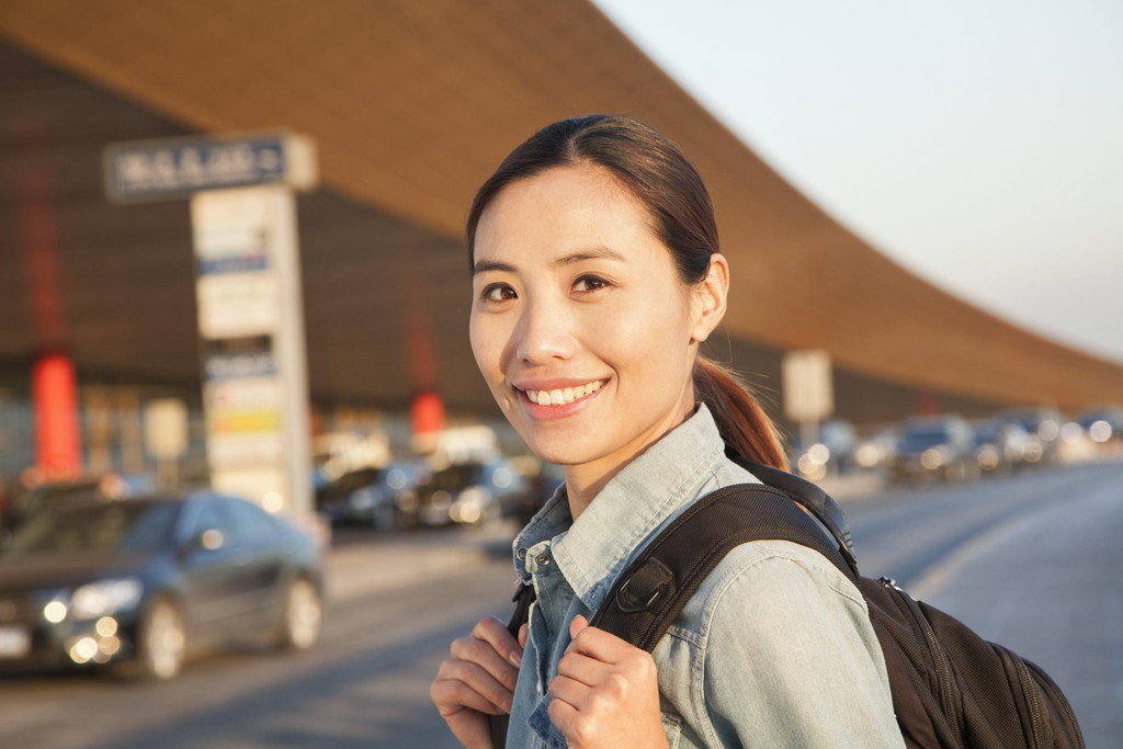 バックパックを背負ったアジア系の若い女性が交通量の多い通りで英語で会話しています。