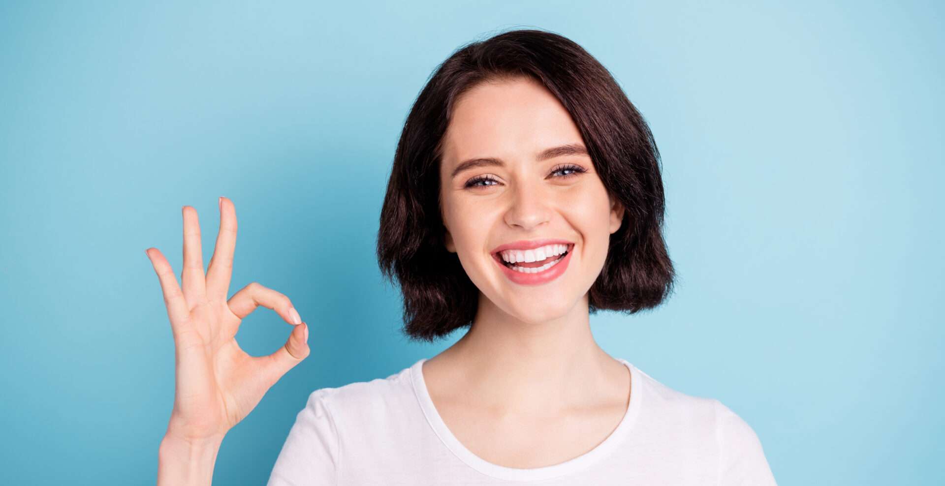 青色の背景に OK サインを出す若い女性。