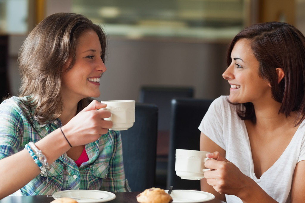 テーブルに座ってコーヒーマグを飲みながら英会話をしている 2 人の女性。