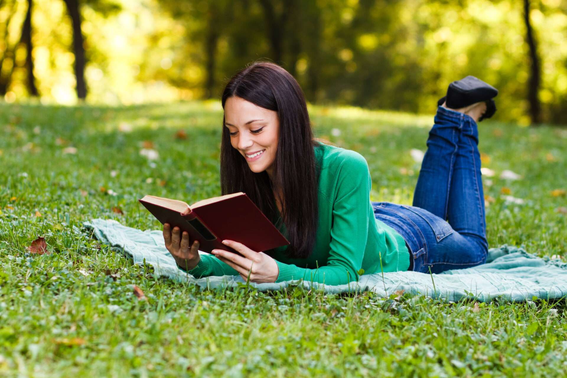 芝生の上で本を読んでいる若い女性。