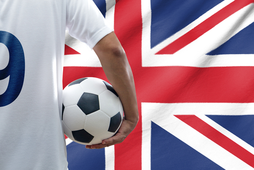 英国国旗の前でサッカー ボールを持ち、他の人と英会話をしている男性。