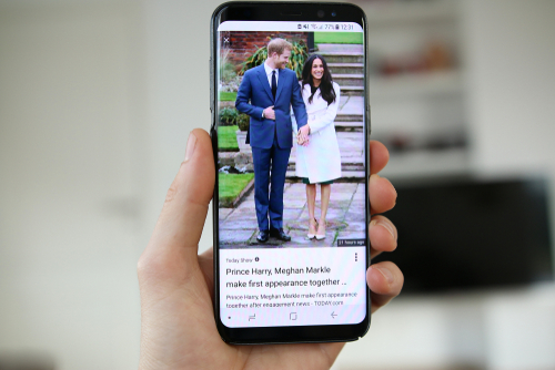ケイトとウィリアムの写真が入った携帯電話を持ちながら英会話をしている人。