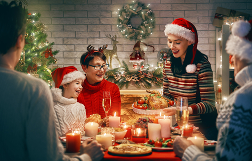 サンタクロースの帽子をかぶって英会話をしながらクリスマスディナーを楽しむ家族。