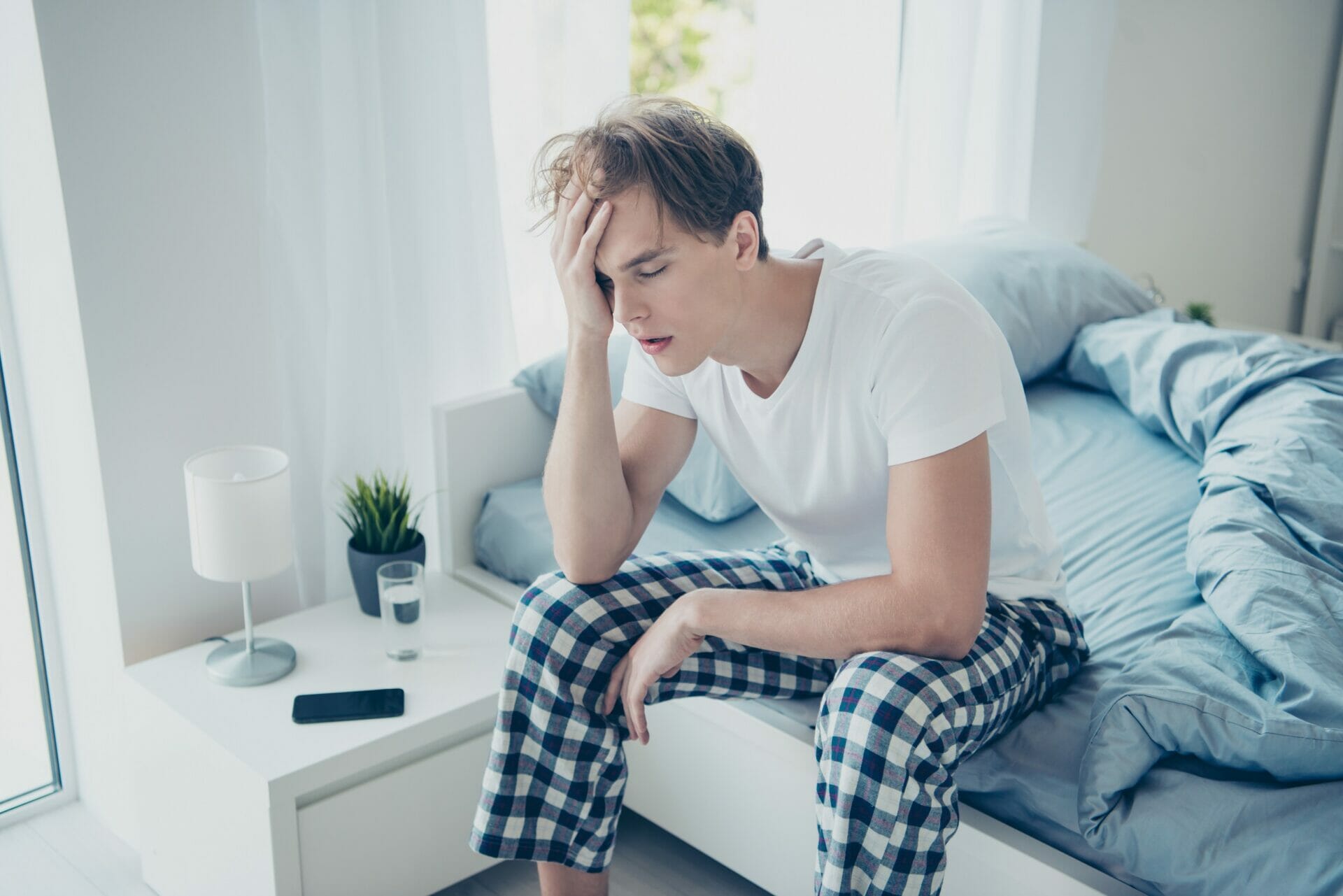 パジャマを着た男性が両手で頭を抱えてベッドに座っています。