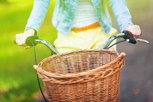 籐のかごを積んで自転車に乗る女性。