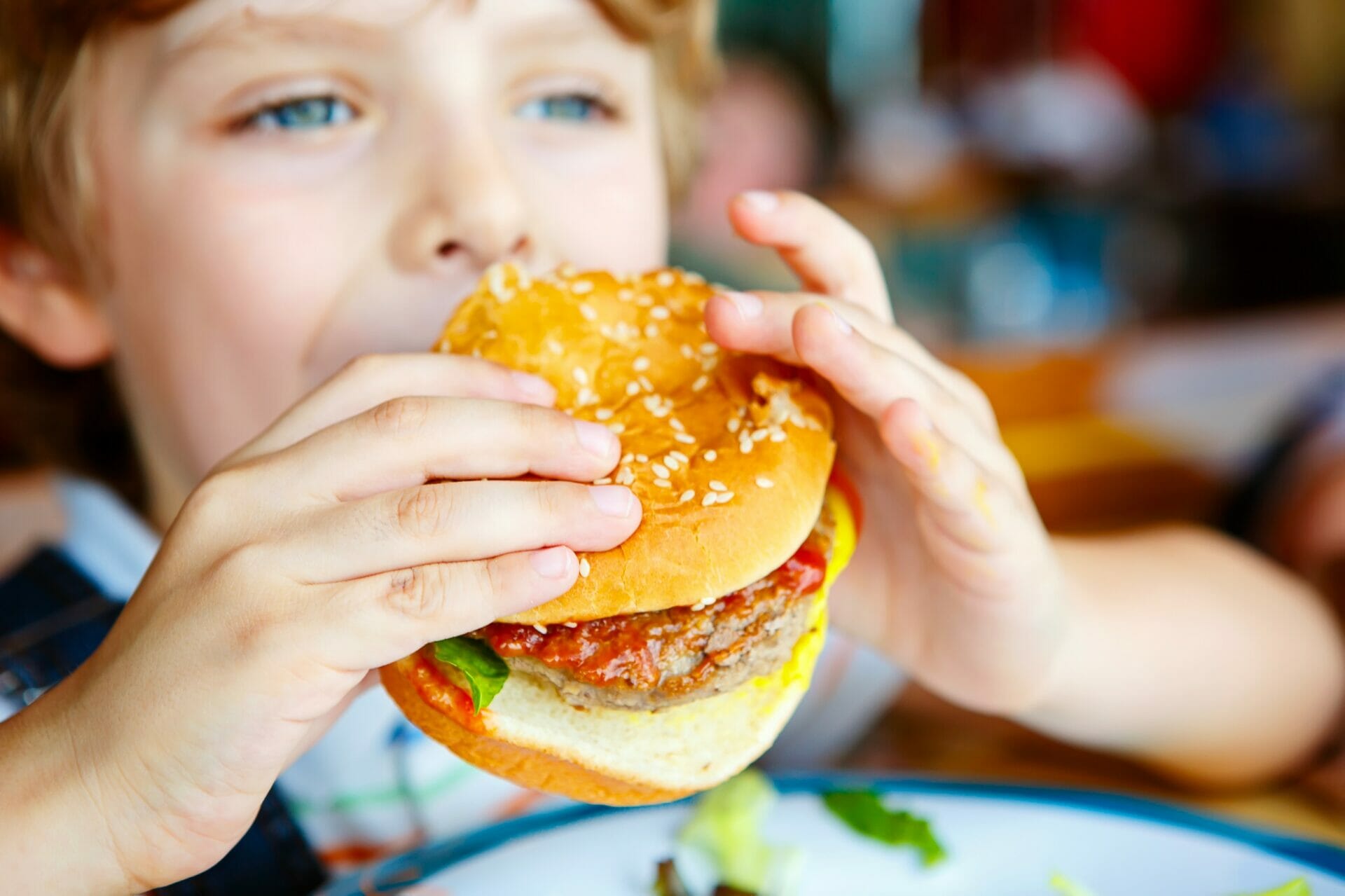 レストランで英語を話しながらハンバーガーを食べる少年。