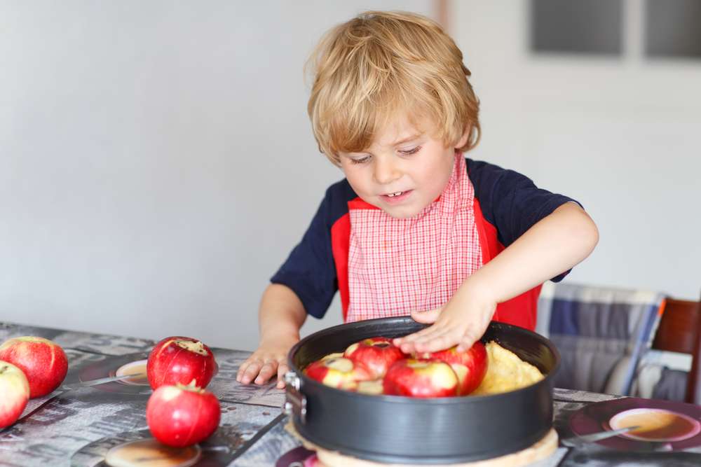 若い男の子が鍋でリンゴを調理しています。