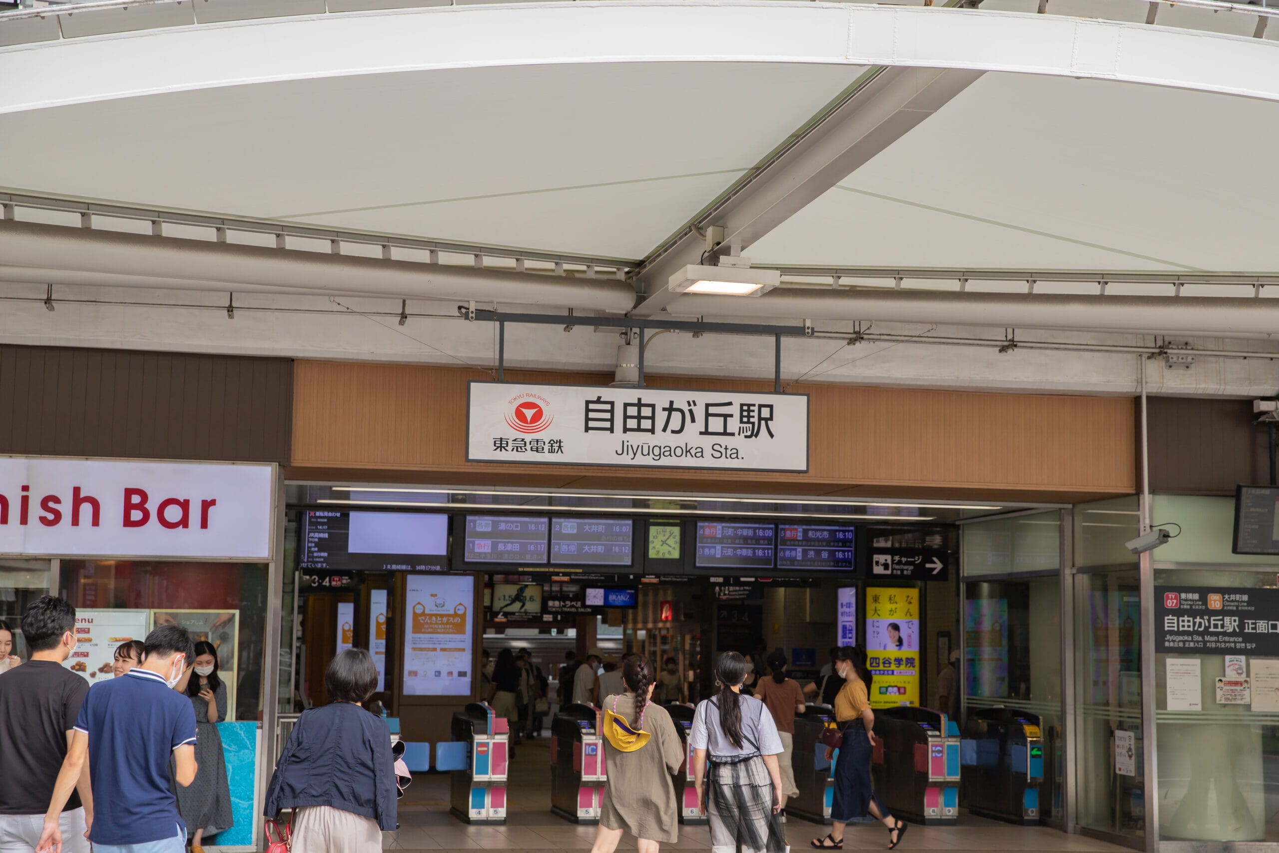日本の自由が丘駅を出入りする人々。英会話スクールマンツーマンのさまざまな標識と上に見える案内板。.