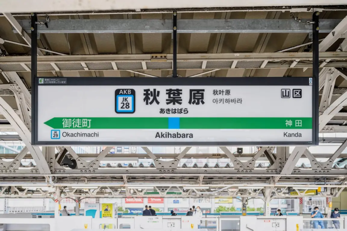 駅のホームにある看板には、英語、日本語、韓国語で「秋葉原」と表示され、御徒町駅と神田駅への道順が書かれている。.
